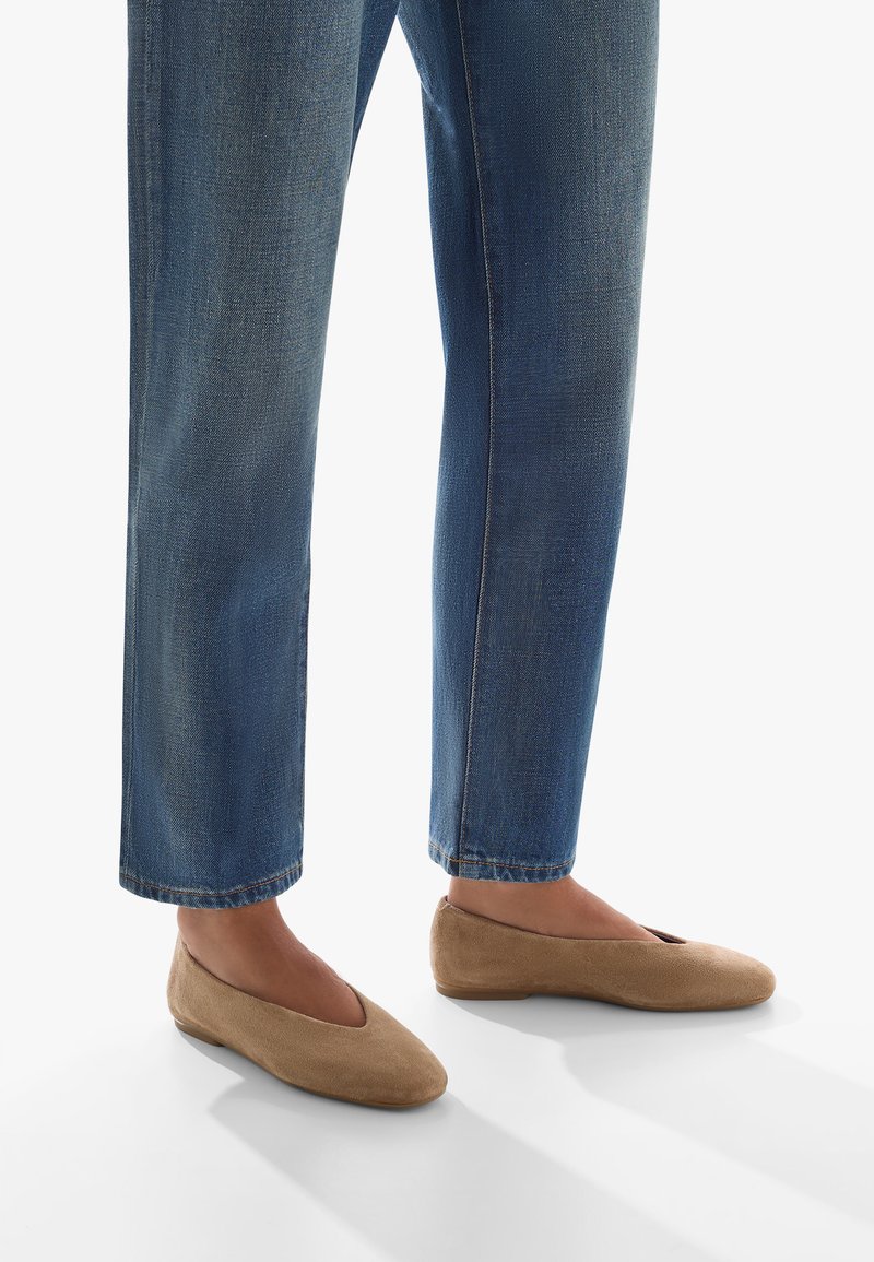 Ballerine in suede beige con punta tonda e dettagli intagliati, abbinate a jeans in denim blu leggermente cropped.