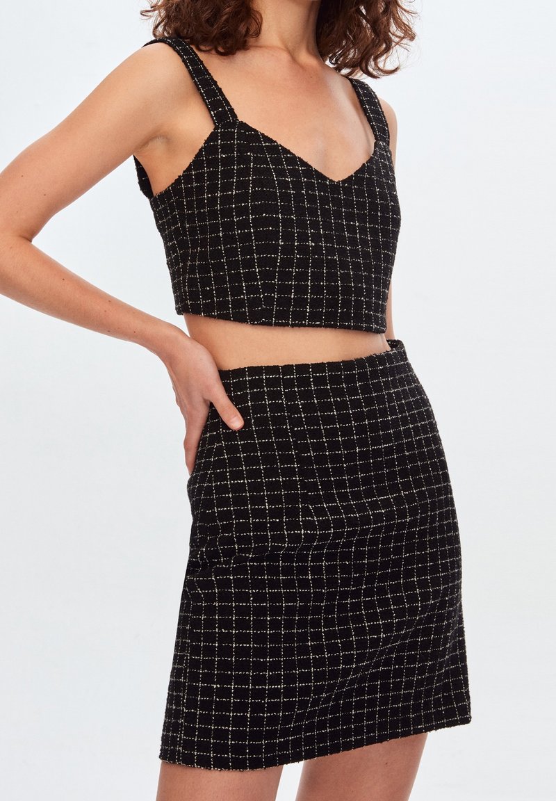Top court à carreaux noir et blanc avec des larges bretelles et un décolleté en V, associé à une jupe mini assortie. Tissu texturé, design ajusté.