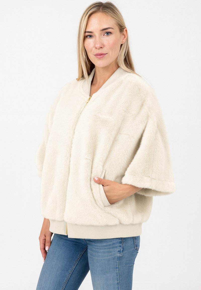 Veste en fausse fourrure crème avec fermeture éclair à l'avant, coupe oversized, manches larges et deux poches latérales. Détails des poignets et du bas côtelés.