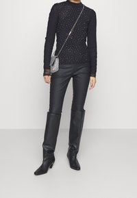 Haut noir à manches longues avec des détails en sequins, associé à un pantalon noir ajusté et des bottes hauteur genou, complété par un petit sac bandoulière en argent.