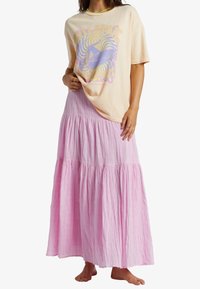 Lichtroze gelaagde maxi-rok van textuurstof, gecombineerd met een zachtbeige graphic t-shirt met kleurrijke teksten en een surfillustratie.