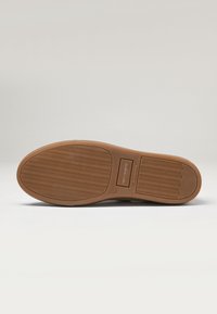 Semelle de chaussure en caoutchouc marron avec un motif en zigzag pour une meilleure traction. Présente une surface texturée, des marquages de marque et une étiquette taille 42.