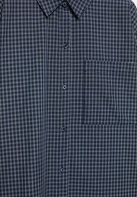 Navy blue checkered shirt with a collar, front buttons, and a left chest pocket. Fabric features small white and beige grid patterns.