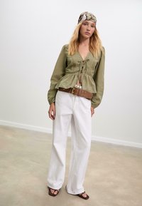 Zelený lněný top s peplum střihem, V výstřihem a detailem na zavazování, kombinovaný s bílými širokými kalhotami a hnědým páskem. Hlavový šátek s květinovým vzorem.