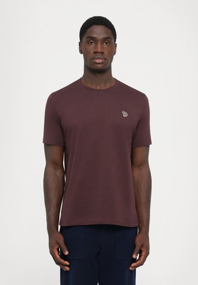 T-shirt à manches courtes, couleur bordeaux, en coton lisse. Col rond avec un petit logo brodé coloré sur la poitrine. Design simple.