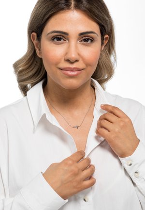 Silberne Kreuzkette an einer filigranen Kette, getragen über einem weißen Kragenhemd; verfügt über subtilen Glanz und minimalistisches Design.