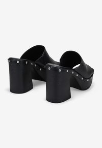 Mules de tacón alto negro de bloque, hechos de material sintético suave. Studs decorativos plateados a lo largo del borde. Diseño de parte trasera abierta y punta redondeada.