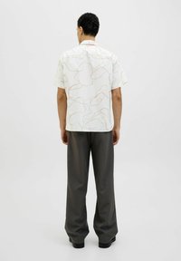 Camisa de manga corta, con un diseño claro y líneas en rosa claro y verde, combinada con pantalones oscuros de corte holgado en gris y zapatos negros.