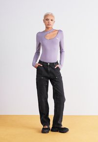Langermet, lyse lilla bodysuit med utskjæring på skulderen, kombinert med høyt liv, svarte vide jeans med frontlommer og sølvdetaljer.