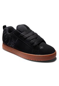 Crne skate cipele s glatkom teksturom i podstavljenim jezikom, opremljene gumenom potplatnom s smešnim potplatima i utisnutim logotipom sa strane.