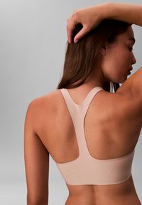 Lyserød sports-bh med bred racerback-design. Glat tekstur, sømløse kanter og en tætsiddende form. Velegnet til træningstøj.