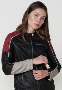 Giubbotto di pelle nera con accenti trapuntati rossi sulle spalle e maniche beige, con zip sul petto e colletto alto.