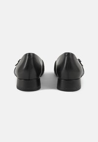 Chaussures en cuir noir avec un petit talon, un bout arrondi et des coutures minimales. Elles présentent un design élégant avec une texture lisse.