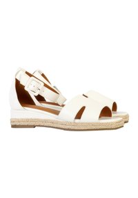 Sandales en cuir blanc avec des découpes, des brides de cheville ajustables et une semelle en jute tressé. Elles possèdent un talon compensé bas pour le confort.