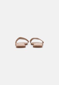 Brune lærsandaler med flad sål og minimalistisk design, der har to opadbuede stropper for støtte og en glat overflade.