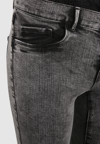 Jeans de mezclilla gris con corte ajustado, bolsillo frontal y una sutil textura. La tela tiene un ligero brillo con un patrón de decoloración.