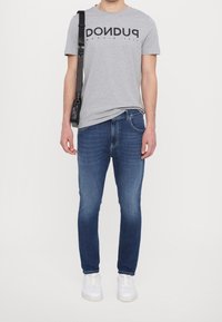 Camiseta de algodón gris con texto en negro, combinada con jeans de mezclilla azul de corte slim y zapatillas blancas. El conjunto incluye un bolso con asa al hombro.