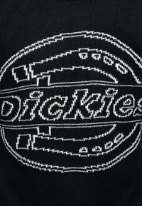 Tissu noir tricoté avec un logo circulaire blanc cousu, présentant le mot « Dickies » en texte stylisé.