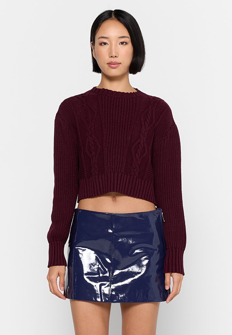 Maglione corto bordeaux con design a trecce, texture a coste sui polsini e sull'orlo, abbinato a una mini gonna blu navy lucida, con zip laterale.