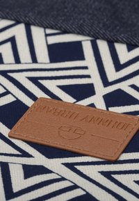 Canvas tyg i marinblått och vitt geometriskt mönster, med en brun läderetikett präglad med "JOHNNY URBAN." Texturerad ytdetalj synlig.