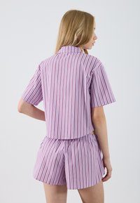 Haut à col et manches courtes, accompagné de shorts assortis en lilas clair avec de fines rayures verticales rouges ; tissu lisse avec une taille élastique.