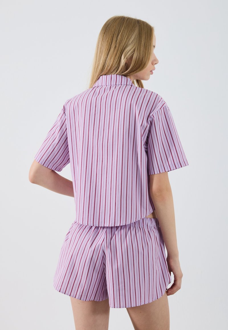 Top a maniche corte con colletto e pantaloni corti abbinati in un viola chiaro con sottili strisce verticali rosse; il tessuto è liscio e presenta una vita elastica.