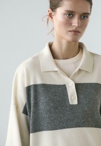 Sweter w stylu polo w kolorach kremowym i szarym, z kołnierzykiem, krótką plisą na guziki i miękką teksturą z poziomym blokowaniem kolorów.