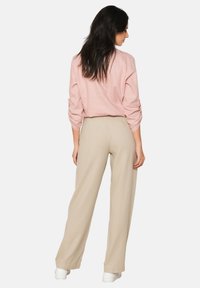 Light pink linen shirt with rolled sleeves paired with beige wide-leg trousers. White sneakers complete the outfit. Smooth textures, casual design.