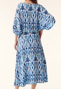 Modré šaty se vzorem, které mají volný, délku po kolena a široké rukávy, kulatý výstřih a jsou vyrobeny z lehké látky.