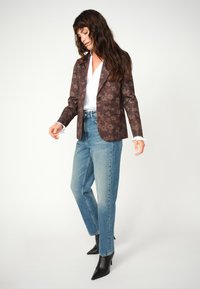Brauner, blumengemusterter Blazer über einem weißen Hemd, kombiniert mit hellblauen, geraden Jeans und schwarzen, spitzen Knöchelstiefeln.