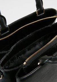 Czarna torebka z teksturowym wykończeniem, złotymi zamkami błyskawicznymi i wnętrzem z materiału z wzorem logo. Dwie krótkie rączki.