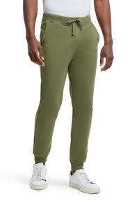 Olijfgroene sweatpants van zachte stof, met een trekband in de taille, zijzakken en taps toelopende benen, gecombineerd met witte sneakers.