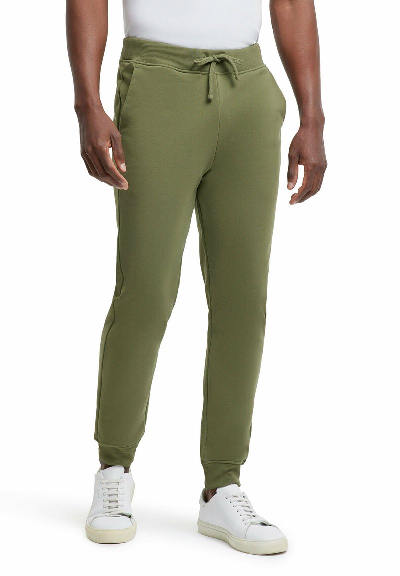 Olijfgroene sweatpants van zachte stof, met een trekband in de taille, zijzakken en taps toelopende benen, gecombineerd met witte sneakers.