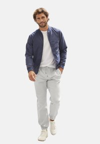 Marine bomberjack met een gladde textuur, witte T-shirt, grijze joggers met elastische boorden en witte sneakers.