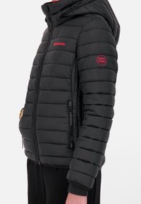 Sort puffert jakke med hætte, der har vandrette syninger, lynlåslommer og rødt logo på brystet og ærmet. Tekstureret finish.