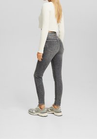 Jeans de mezclilla gris de talle alto con corte slim, diseño de cinco bolsillos y acabado desgastado, combinados con una camiseta de manga larga de canalé blanca y zapatillas grises.