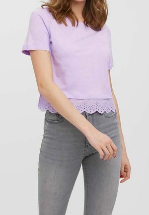 Lys lilla cropped t-shirt i blød bomuld med korte ærmer, der har en bølget øjelet blonderkant. Parret med grå jeans.