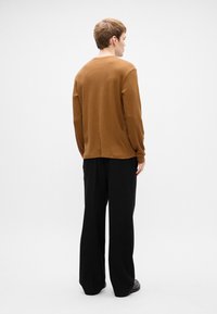 Καφέ μακρυμάνικο πουκάμισο με υφή, συνδυασμένο με φαρδιά μαύρα παντελόνια. Το πουκάμισο έχει στρογγυλή λαιμόκοψη και ελαφρώς κατεβασμένους ώμους.