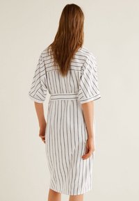 Vestido blanco con rayas verticales oscuras, mangas cortas, cintura atada y corte a la altura de la rodilla. Textura de tela suave con un ajuste relajado.