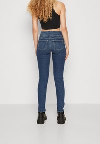 Jeans de denim azul skinny con una cintura de media altura, que cuentan con bolsillos traseros y una textura suave. Combinados con botas de plataforma negras.