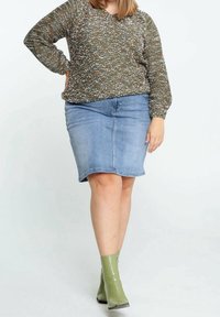 Zielony sweter z dzianiny w cętkowanym wzorze, w połączeniu z jasnoniebieską spódnicą dżinsową. Modelka nosi błyszczące zielone botki za kostkę.