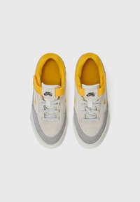 Nike-sneakers med en grå mockaöverkåt, en gul mesh-krage och vit gummisula. Designen inkluderar snörning och en mellanhög silhuett.