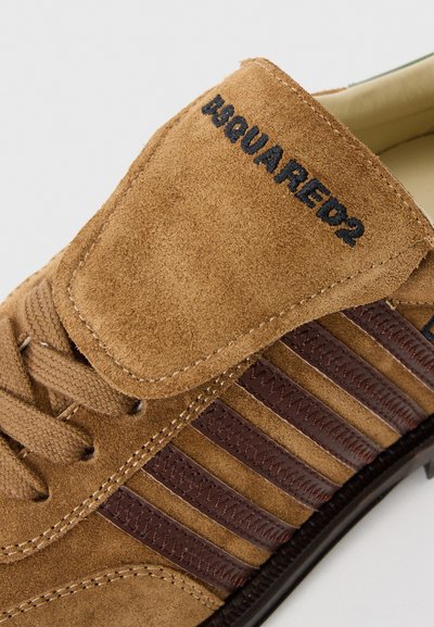 Bruna mockaskor med bruna läderremsor, snören och en vadderad tunga som har svart "DSQUARED2" text. Strukturerad yta med kontrasterande detaljer.