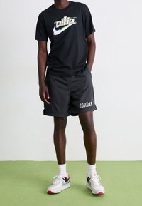 Camiseta negra de manga corta con el logo colorido de Nike y el texto "Just Do It", combinada con pantalones cortos negros que tienen "JORDAN" en blanco, todo sobre un fondo claro.