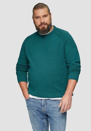 Pull en tricot teal avec un motif texturé, doté de poignets et d'un col côtelés. Associé à un jean en denim bleu clair.