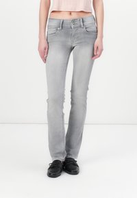 Grå denimjeans med slim fit, to front lommer, to baklommer og to-knaps lukking. Brukt med svarte sko.