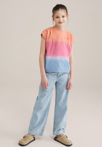 Trumpas rankovėmis, gradientinė T-shirt su oranžinėmis, rožinėmis ir mėlynomis tonomis. Suporuota su šviesiai mėlynomis dryžuotomis plačiomis kelnėmis ir béžiniais slip-on batais.