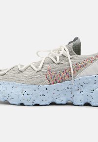 Šedá pletená teniska s texturovanou svrchní částí, barevně vyšívaným logem Swoosh a modrou podrážkou se skvrnami. Má bílé tkaničky a polstrovaný límec.