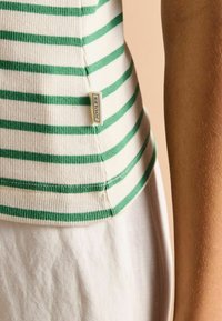 White ribbed tank top with green horizontal stripes, featuring a side seam tag. The fabric is textured with a soft, stretchy appearance.