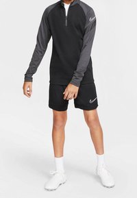 Svart zip hoodie med grå ärmar, tillsammans med svarta shorts. Har Nike-loggor och vita sportskor med vita strumpor.